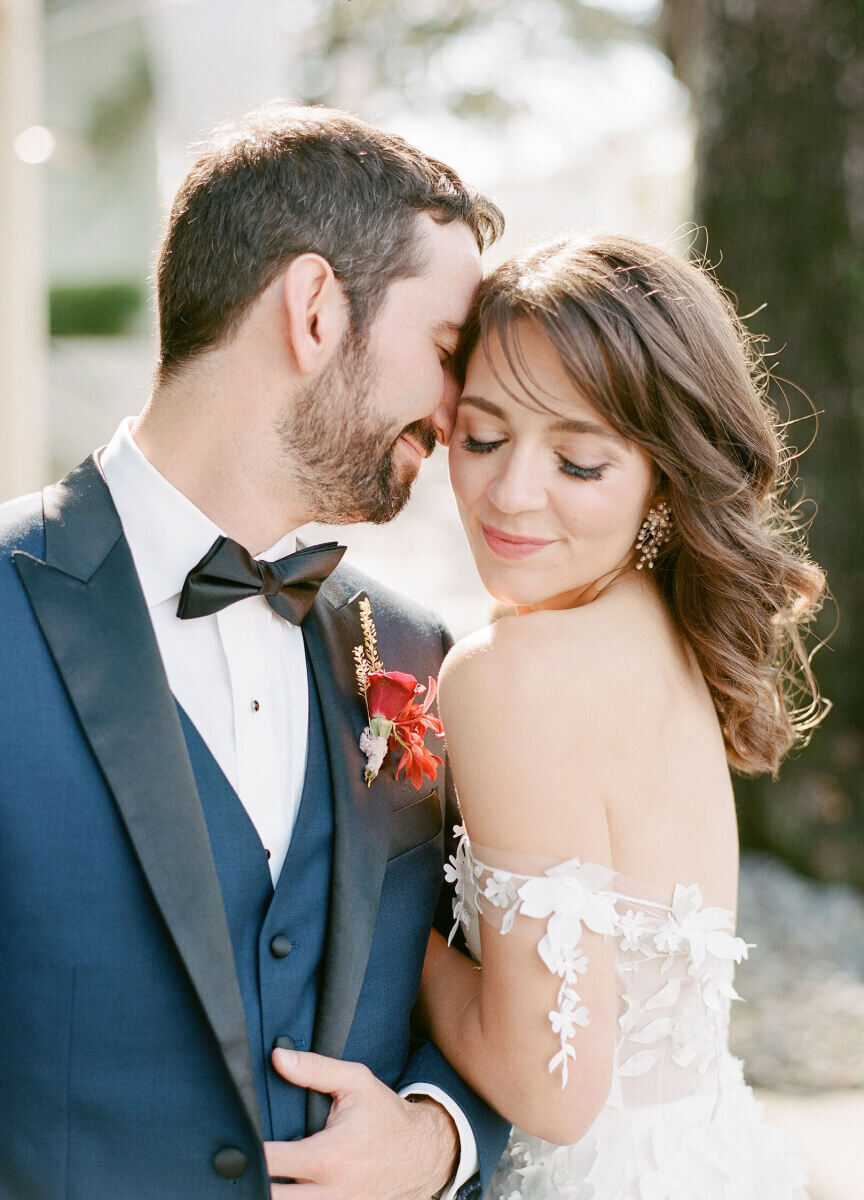 A groom in a blue tuxedo nuzzles into his bride who wears an off-the-shoulder lace dress at their art-inspired wedding.