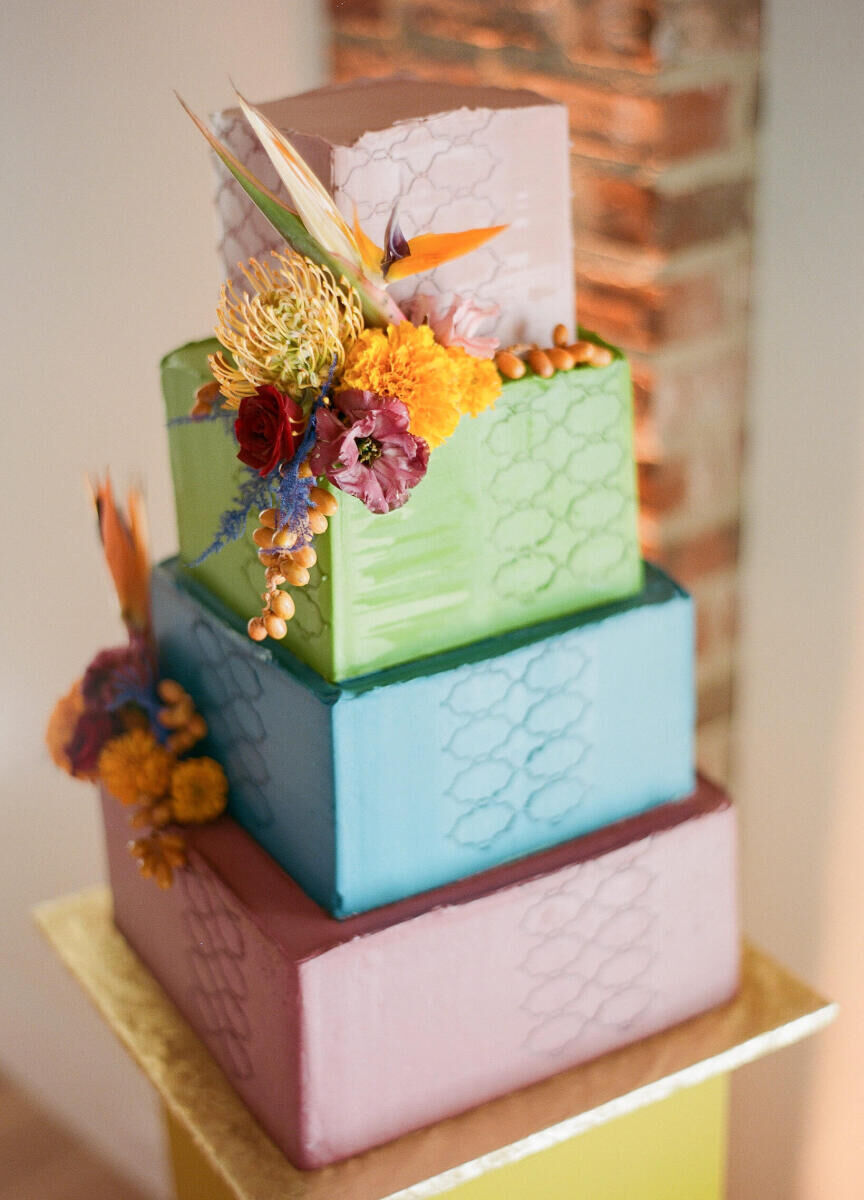 The wedding cake at an art-inspired wedding was four square tiers of pink, green, and blue buttercream-covered sweetness, decorated with patterned impressions, textured icing, and fresh flowers.