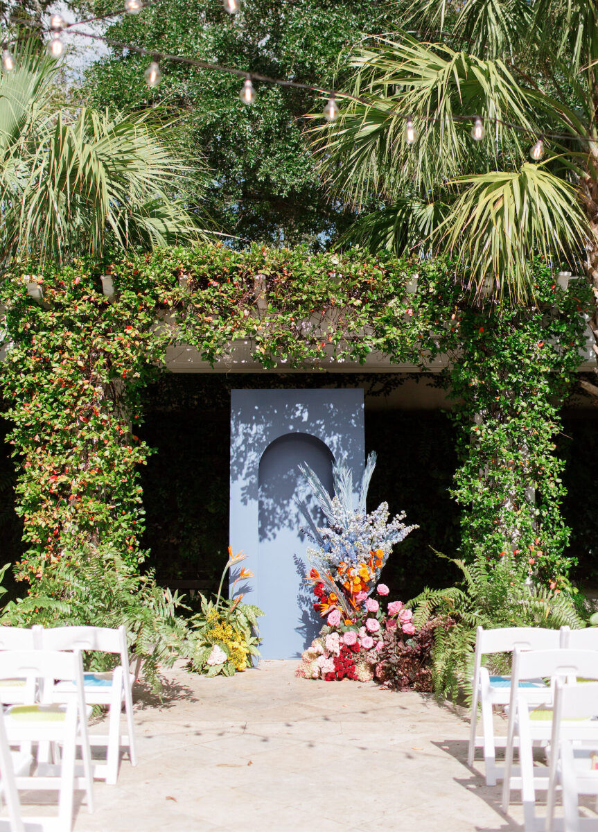 An art-inspired wedding ceremony centered on a blue arched panel decorated with asymmetrical and colorful floral arrangements.
