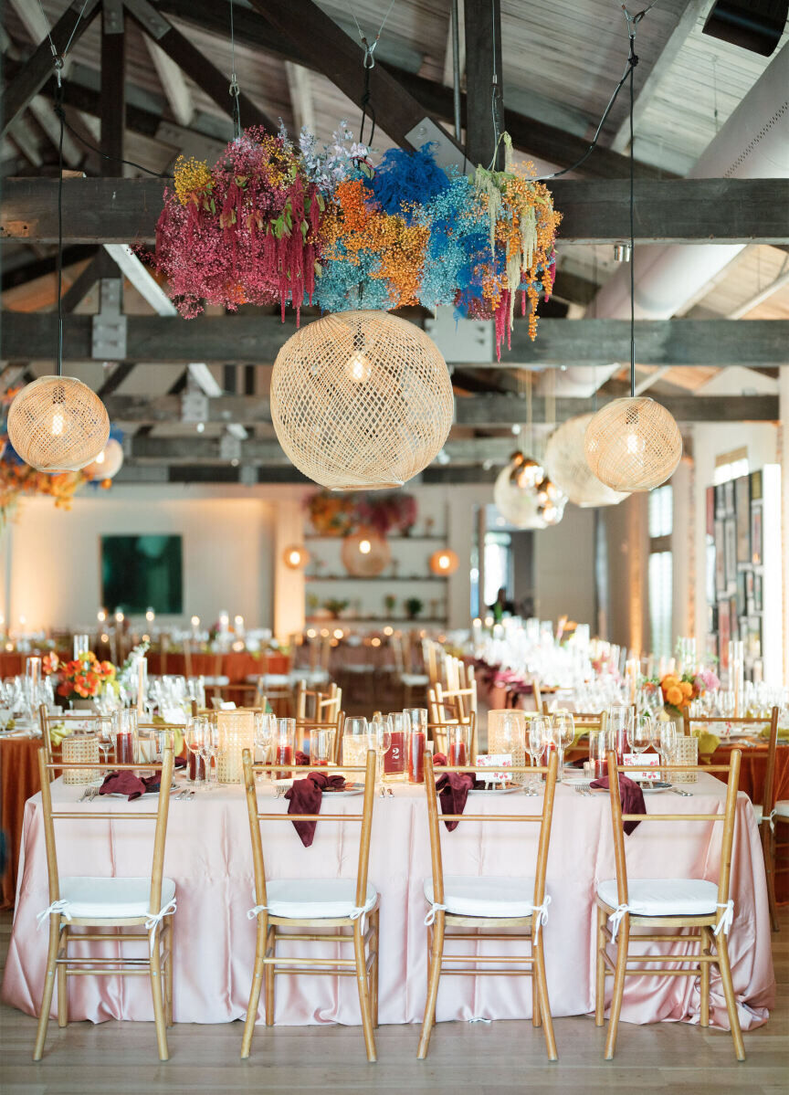 Long tables covered with pink satin tablecloths and burgundy velvet napkins were set with modern wood chairs at an art-inspired wedding reception.