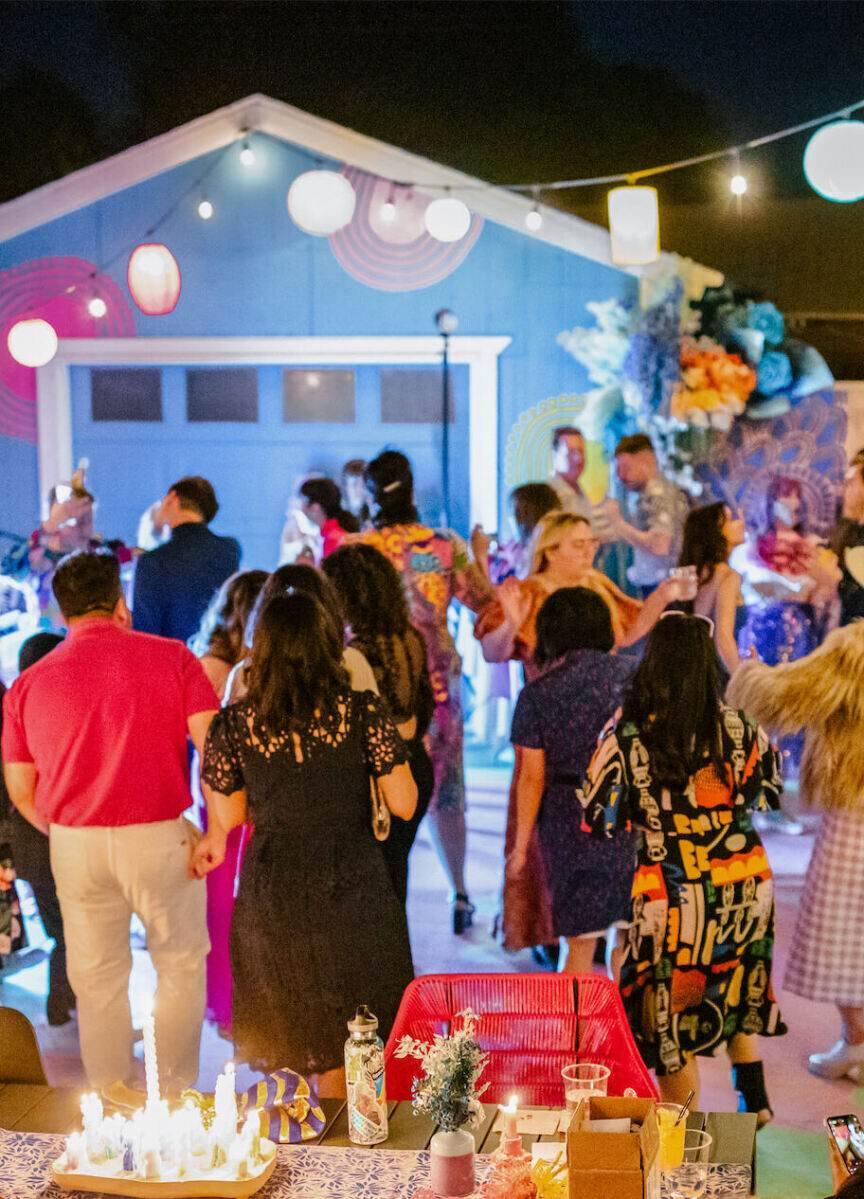 A vibrant outdoor wedding reception, with lanterns and string lights glowing overhead.