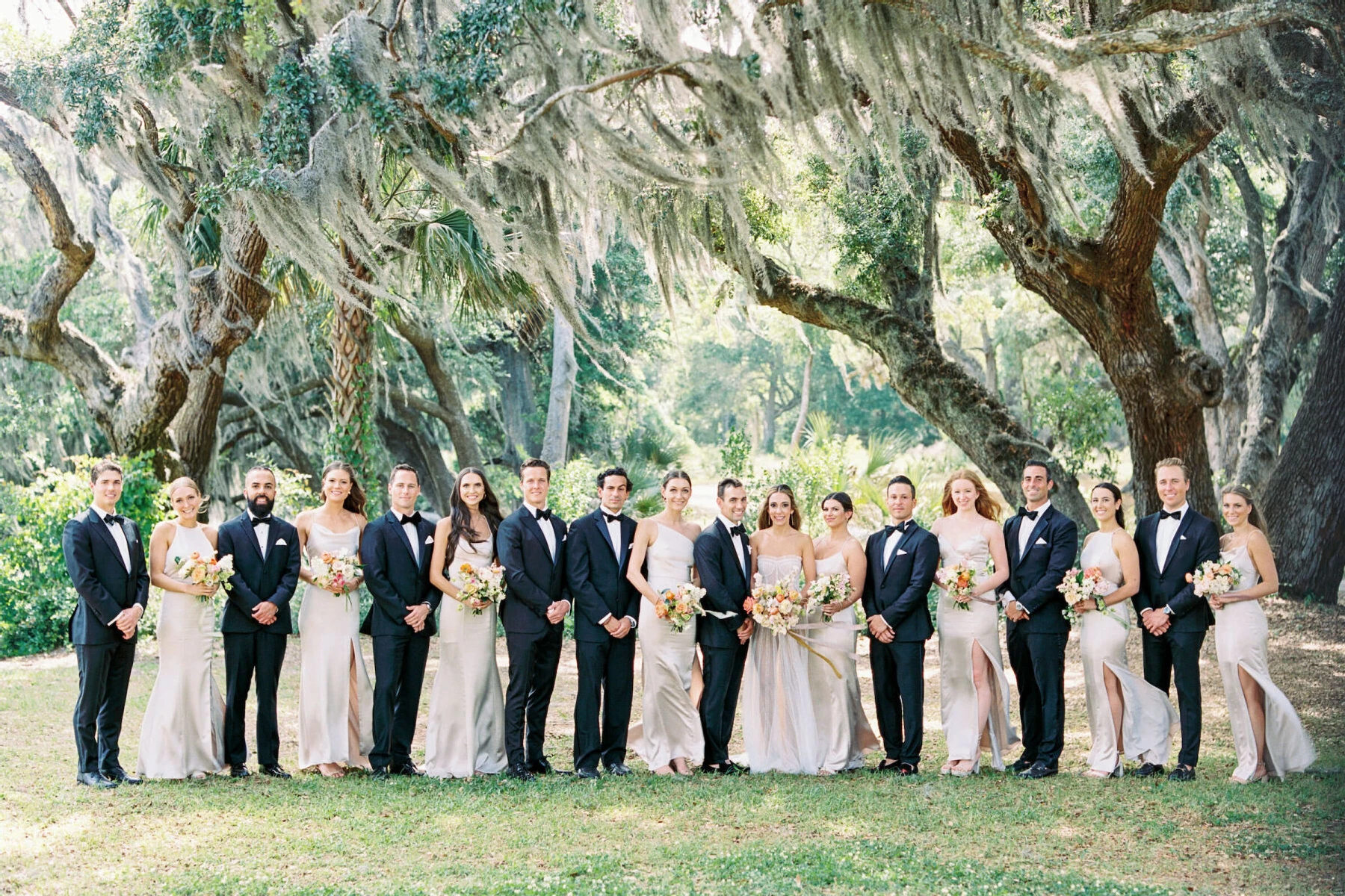 Groomsmen in tuxedos and bridesmaids in champagne dresses surround a bride and groom in South Carolina at an elegant spring wedding.